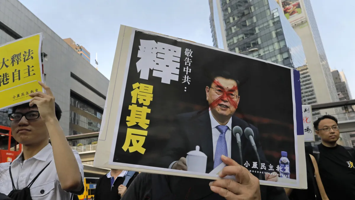 香港本土派民眾6日走上街頭「反釋法」,抗議北京當局試圖藉由人大釋法,封殺具「港獨」色彩的立法會議員,海報上的人像即為人大委員長張德江。(AP)