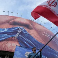 2026年5月6日、イランの首都テヘラン中心部の広場で、国旗を振り政府への支持を表明する男性。広場には、ホルムズ海峡と、唇を縫い合わされた米大統領のドナルド・トランプ氏が描かれた看板が設置されている。(写真/AP通信提供) 2026年5月6日、イランの首都テヘラン中心部の広場で、国旗を振り政府への支持を表明する男性。広場には、ホルムズ海峡と、唇を縫い合わされた米大統領のドナルド・トランプ氏が描かれた看板が設置されている。(写真/AP通信提供)