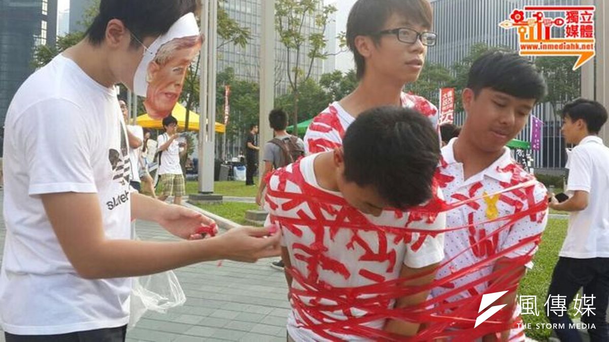 城大政改關注組成員身穿校服,被戴面具的人貼滿紅膠紙,象徵學生被中共政權染紅,在民主路上被拉倒。(取自香港獨立媒體網) 城大政改關注組成員身穿校服,被戴面具的人貼滿紅膠紙,象徵學生被中共政權染紅,在民主路上被拉倒。(取自香港獨立媒體網)