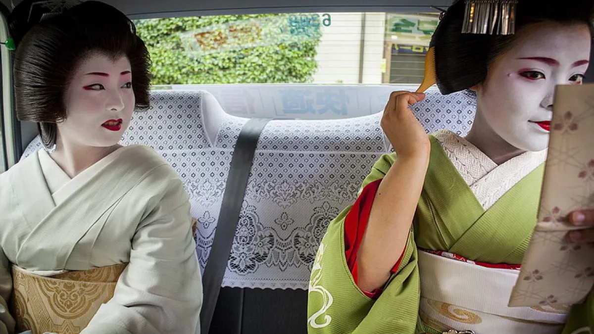一位經驗豐富的藝妓對著鏡子調整妝容,她們正乘坐出租車趕往工作的地方。(圖/言人文化提供)