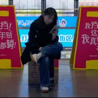 A young woman scrolls her phone at a shopping mall in Beijing, with a banner promoting positive attitudes visible in the background. (AP) A young woman scrolls her phone at a shopping mall in Beijing, with a banner promoting positive attitudes visible in the background. (AP)