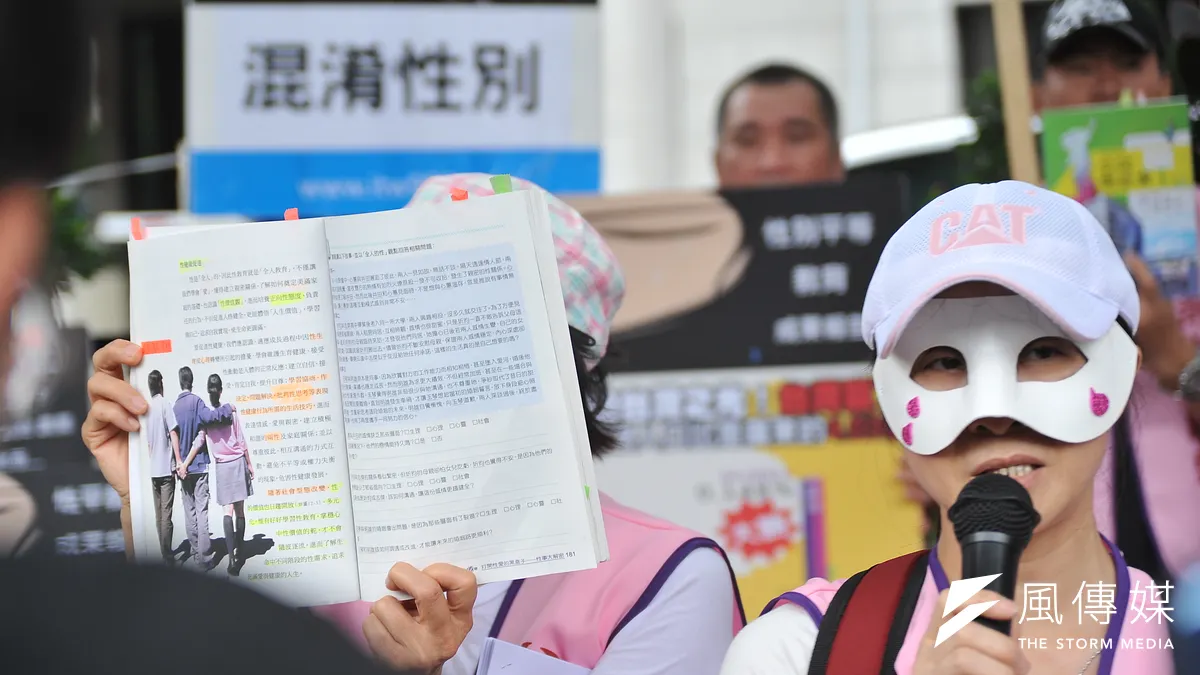 媽媽盟「媽媽最大的憂慮-不當性平教育退出校園」記者會,一位戴面具的家長,並指課本上一張3人並肩(兩男一女)的圖,是教導「多P」行為。(甘岱民攝) 媽媽盟「媽媽最大的憂慮-不當性平教育退出校園」記者會,一位戴面具的家長,並指課本上一張3人並肩(兩男一女)的圖,是教導「多P」行為。(甘岱民攝)