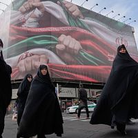 2026年1月14日、イランの首都テヘランで、通りを歩く女性たちの背後にイラン国旗を握りしめる愛国主義的な巨大ポスターが掲げられている。(AP通信) 2026年1月14日、イランの首都テヘランで、通りを歩く女性たちの背後にイラン国旗を握りしめる愛国主義的な巨大ポスターが掲げられている。(AP通信)