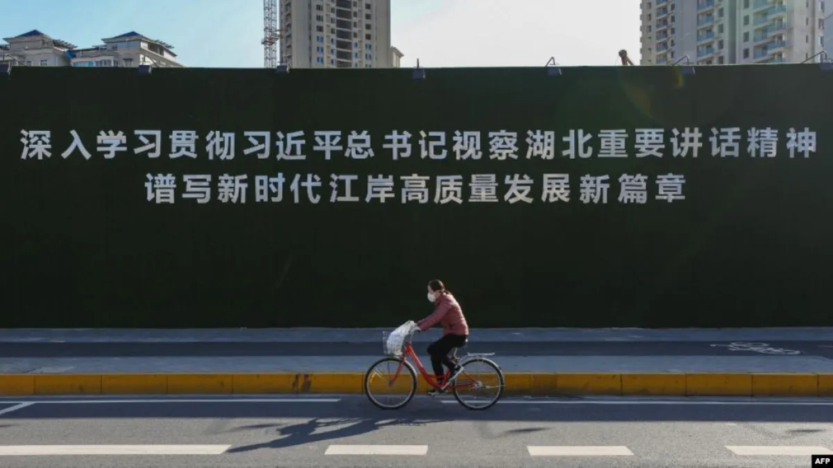 一名戴著口罩的婦女從武漢街頭一幅宣傳習近平湖北講話的大標語前騎車而過。(美國之音)