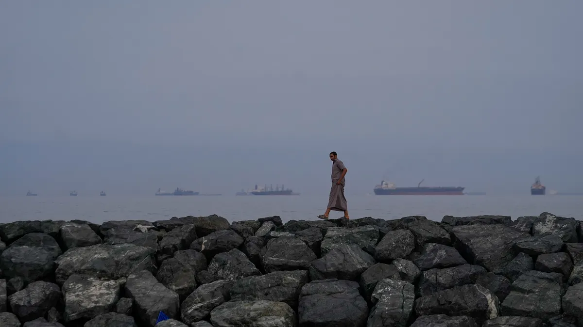 2026年3月11日,阿聯酋霍爾費坎一名男子,沿著荷莫茲海峽的海岸行走,遠處可見油輪和貨輪。(美聯社)