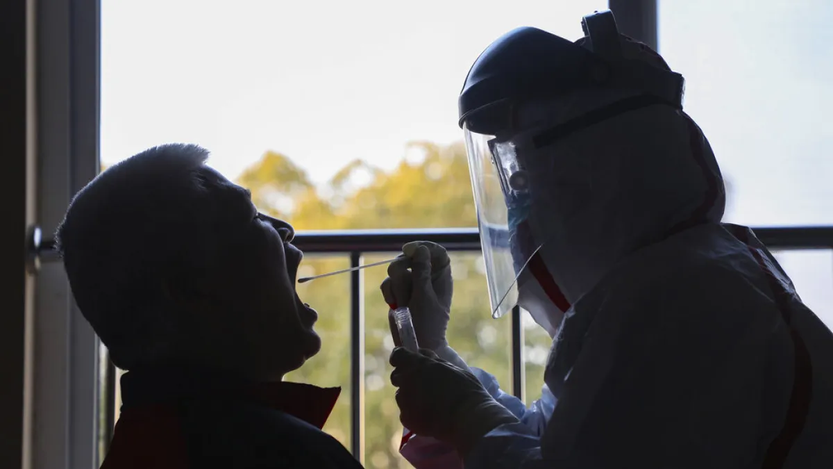 武漢一名穿著全套防護服的工作人員正在為隔離民眾採樣。(美聯社)