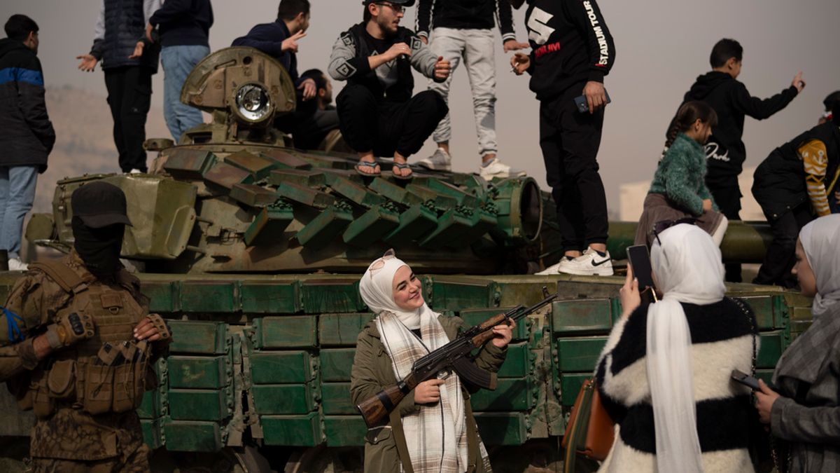 2024年12月11日。敘利亞大馬士革,一名婦女拿著從敘利亞叛軍那裡借來的步槍,在一輛留在街頭的政府軍坦克旁邊合影。(AP) 2024年12月11日。敘利亞大馬士革,一名婦女拿著從敘利亞叛軍那裡借來的步槍,在一輛留在街頭的政府軍坦克旁邊合影。(AP)