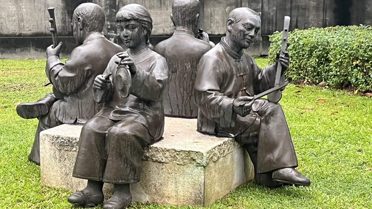 中型作品「八音」展示於板橋故事屋旁,老樹下,四名身穿客家傳統服飾的樂師,手執各式樂器,栩栩如生演奏古調。(圖/新北市政府文化局)