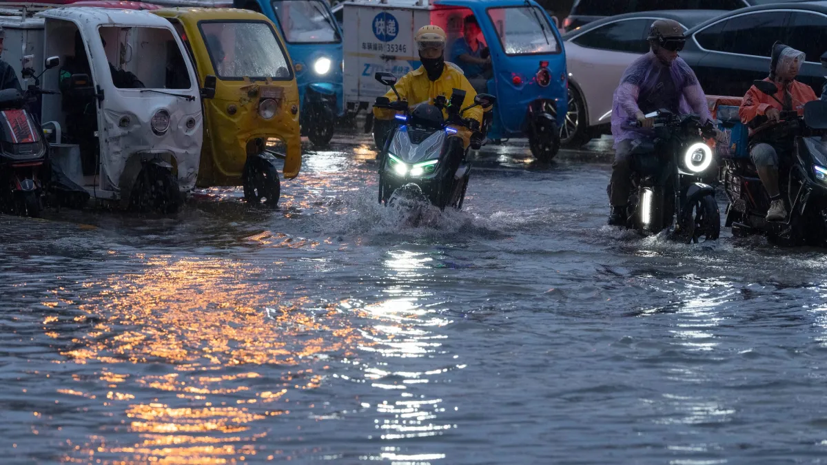 2026年7月10日,北京因為暴雨淹水,騎士幾乎是在水中騎車。(美聯社)