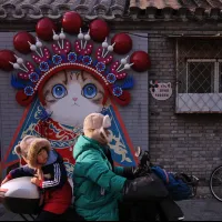 2025年12月28日,中國北京,一名男子騎著電動自行車載著孩子,行經胡同巷弄中一幅結合京劇元素的貓咪彩繪牆。(美聯社) 2025年12月28日,中國北京,一名男子騎著電動自行車載著孩子,行經胡同巷弄中一幅結合京劇元素的貓咪彩繪牆。(美聯社)