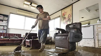 日本九州地區豪雨成災,許多民宅泡在水中,一位災民正在清理屋內的泥濘(AP)