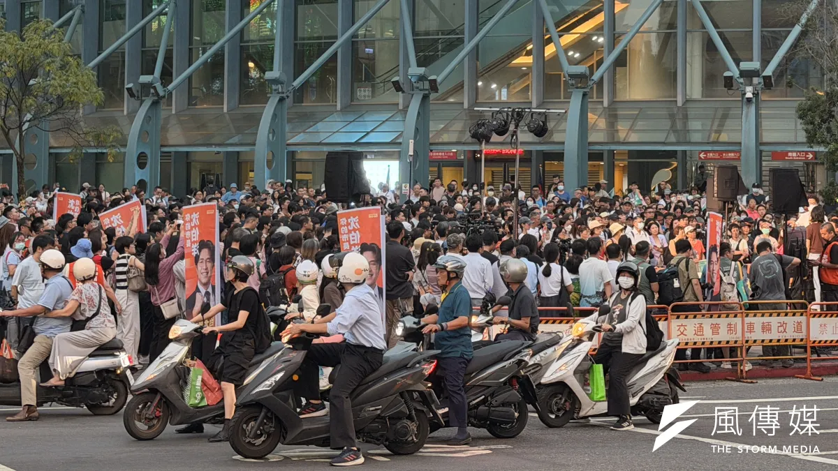 民進黨台北市長參選人沈伯洋在台北小巨蛋外舉辦「肥皂箱」活動,路過機車騎士停等紅綠燈期間轉頭張望。(鍾秉哲攝)