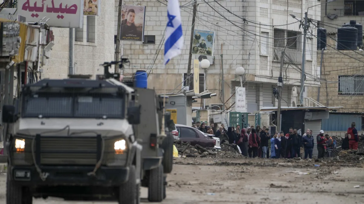 2025年1月22日。在約旦河西岸(West Bank)城市哲寧(Jenin)難民營,巴勒斯坦人看著一台以色列軍用車輛。(AP)