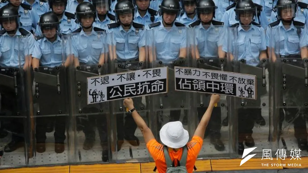 爭取民主自由的香港民眾,在鎮暴警察前方高舉標語牌(美聯社)