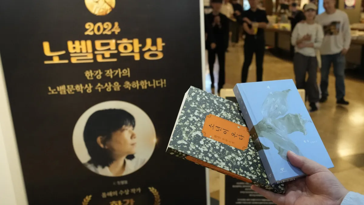 2024年10月11日,韓國民眾在搶買到諾貝爾文學獎得主韓江的作品後,把書本與韓江簡介立牌合影。(美聯社)