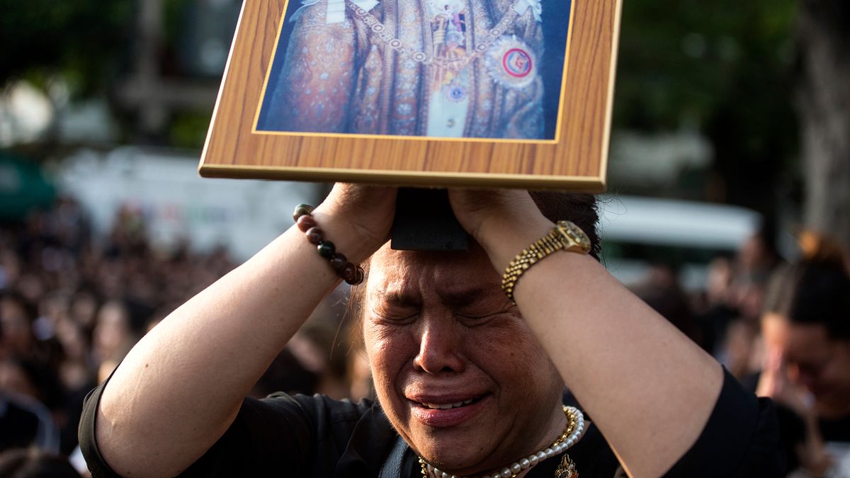 一位泰國婦女14日拿著駕崩泰王蒲美蓬的遺照默禱,等待運送泰王遺體的車隊經過。(美聯社) 一位泰國婦女14日拿著駕崩泰王蒲美蓬的遺照默禱,等待運送泰王遺體的車隊經過。(美聯社)