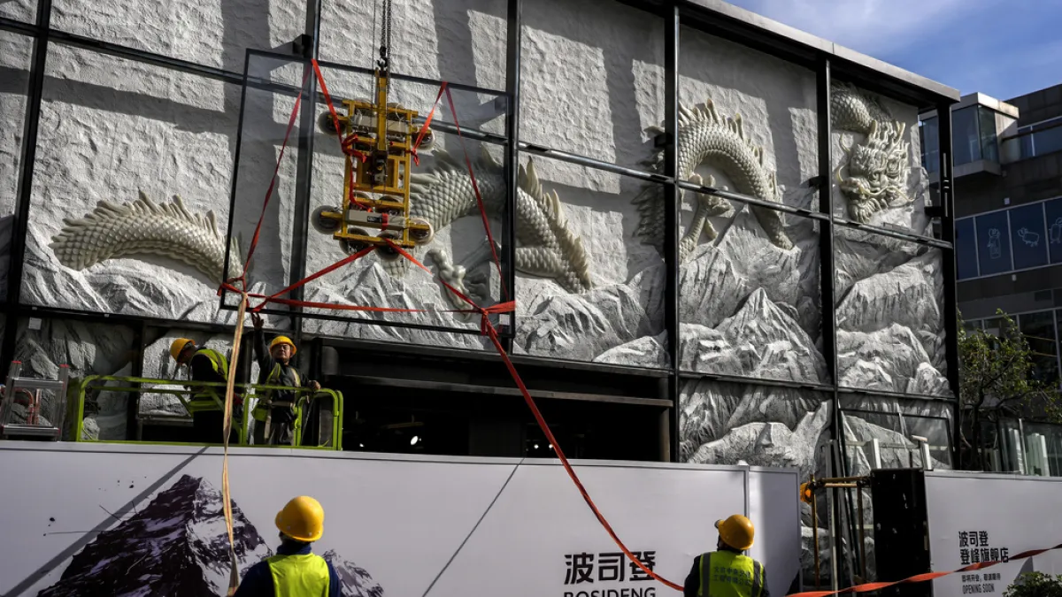 2024年11月4日。北京。在一家購物賣場附近,工人們準備在一家翻新的時尚精品店外安裝一個展示有龍的藝術雕塑的玻璃板。中國經濟、工人(AP)