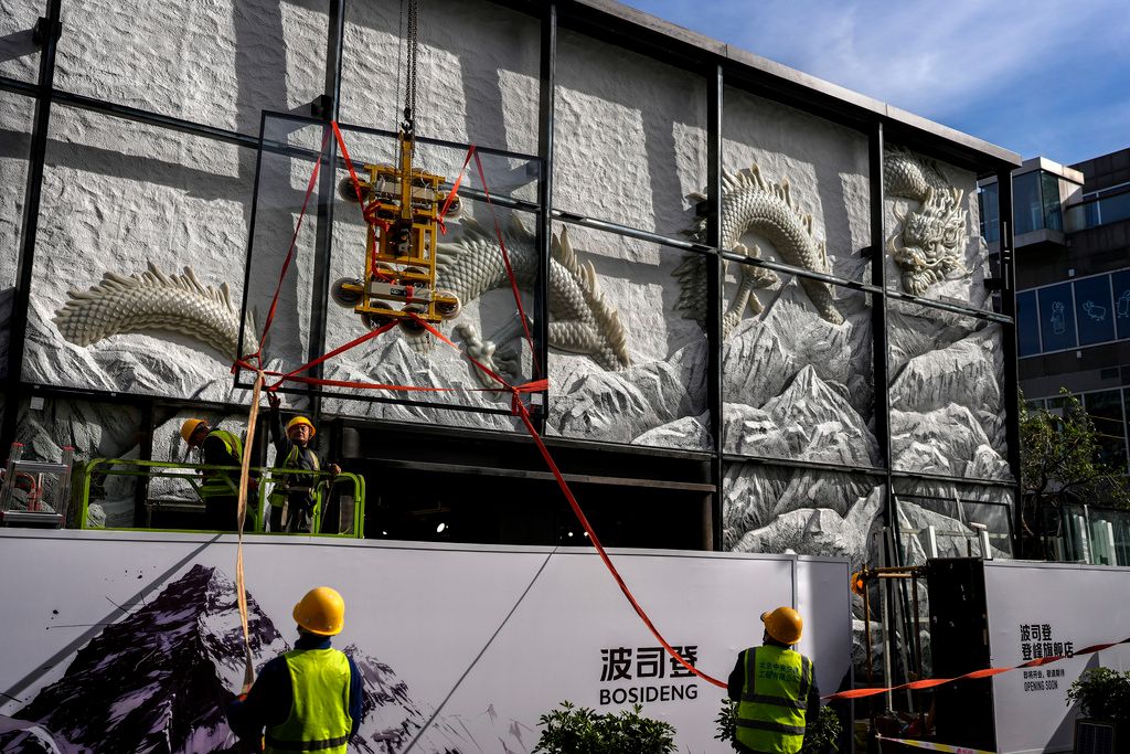 2024年11月4日。北京。在一家購物賣場附近，工人們準備在一家翻新的時尚精品店外安裝一個展示有龍的藝術雕塑的玻璃板。中國經濟、工人（AP）