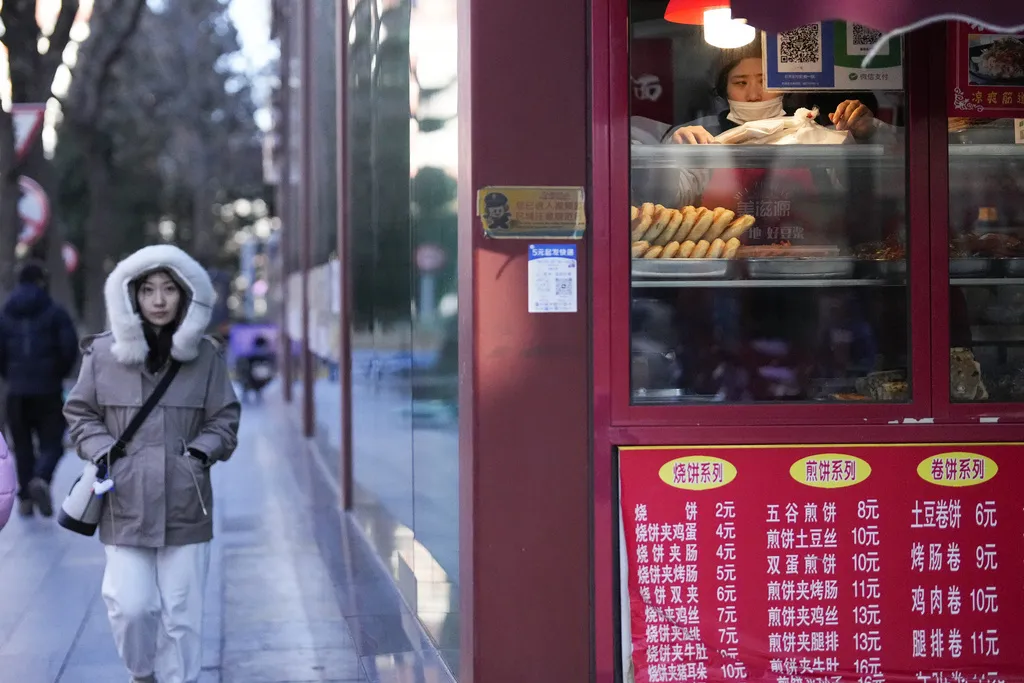 2025年1月8日。中國北京，一個寒冷的早晨，一名員工在餐廳裡擺設食物，而另一名婦女正在散步。 （AP）中國經濟
