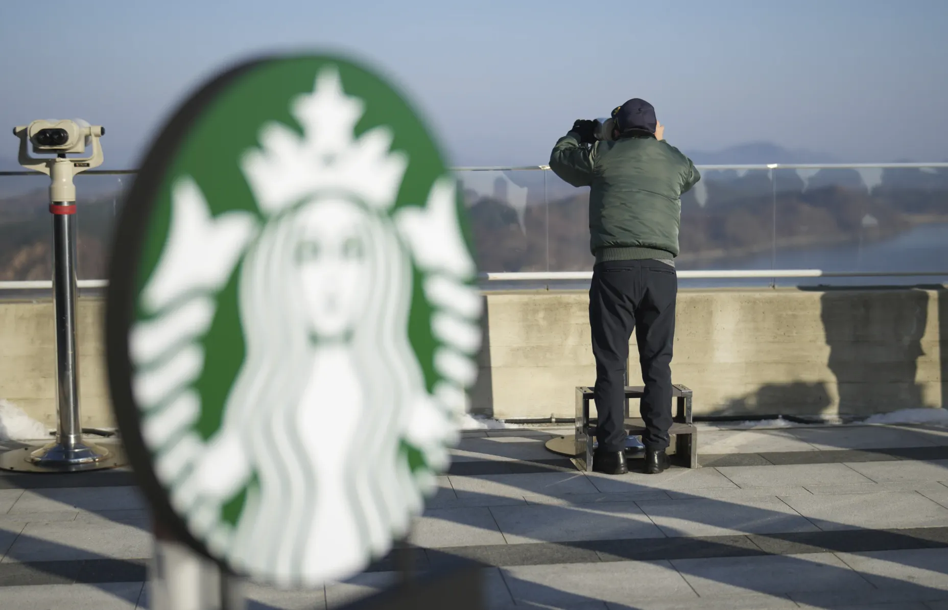 位在南北韓邊界、距離北韓僅1.4公里星巴克門市，一名遊客透過望遠鏡窺視北韓。（美連社）