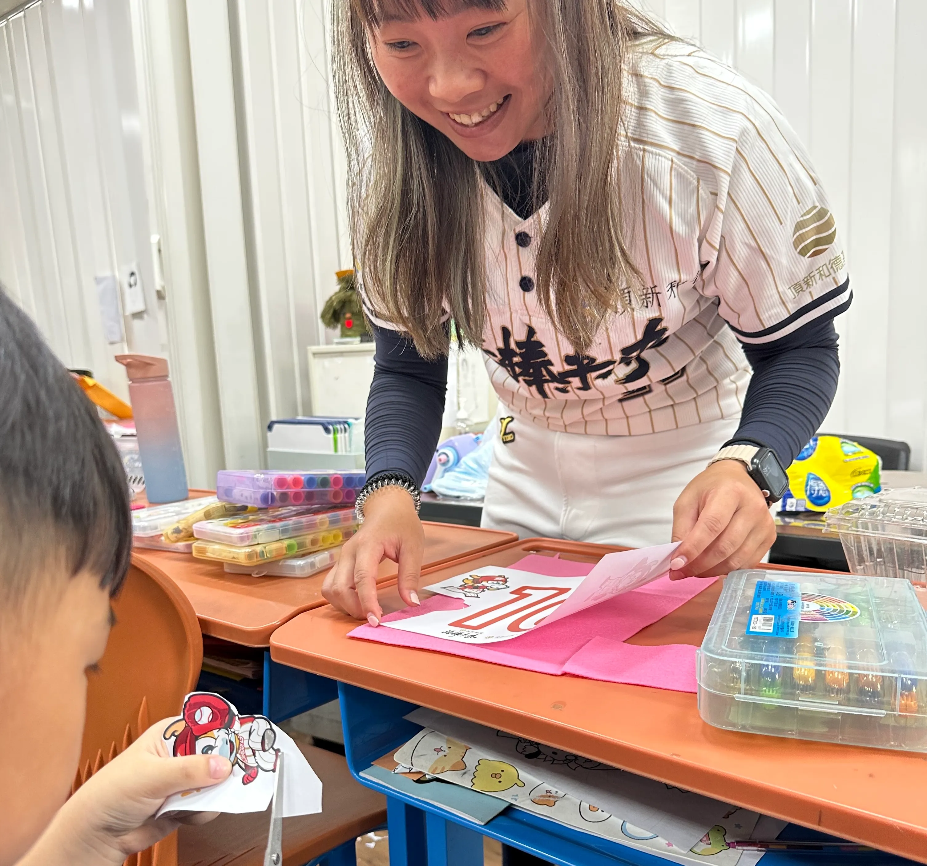 學童在老師和志工的陪伴下一同製作專屬棒球背心，設計屬於自己的球衣背號。(頂新和德文教基金會提供) 