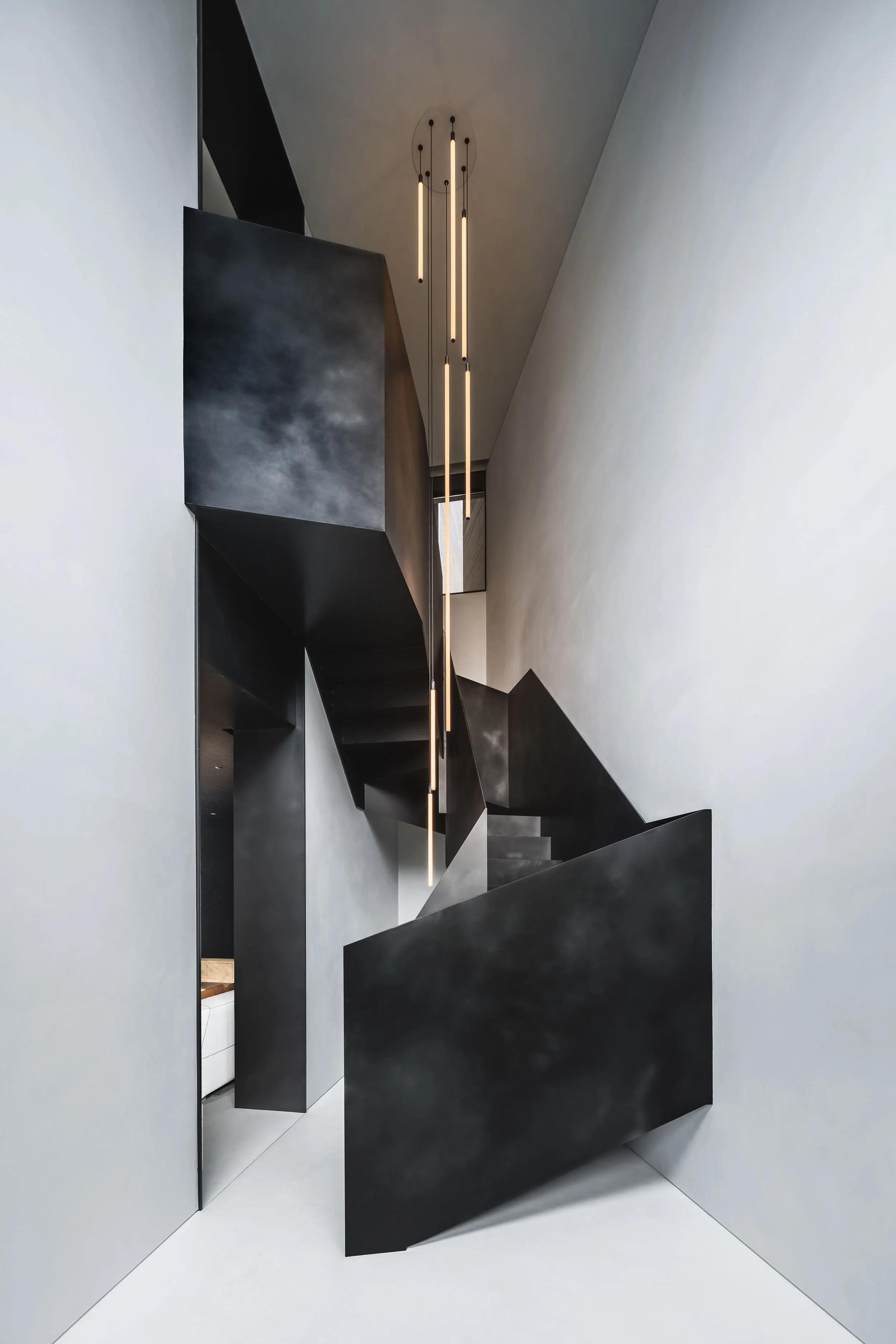 由折疊鋼板打造的雕塑感樓梯，靈感來自摺紙藝術，上方懸掛充滿特色的細長吊燈。（圖／Aston Martin）