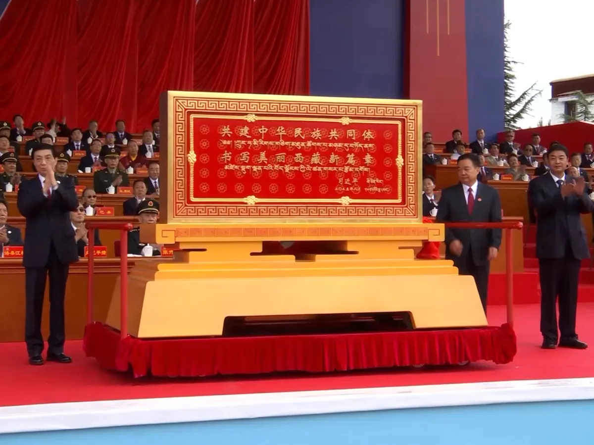 王滬寧（左一）在西藏自治區成立60週年慶祝大會上，向西藏自治區贈送中國國家主席習近平題詞的賀匾。 （央視新聞影片截圖）