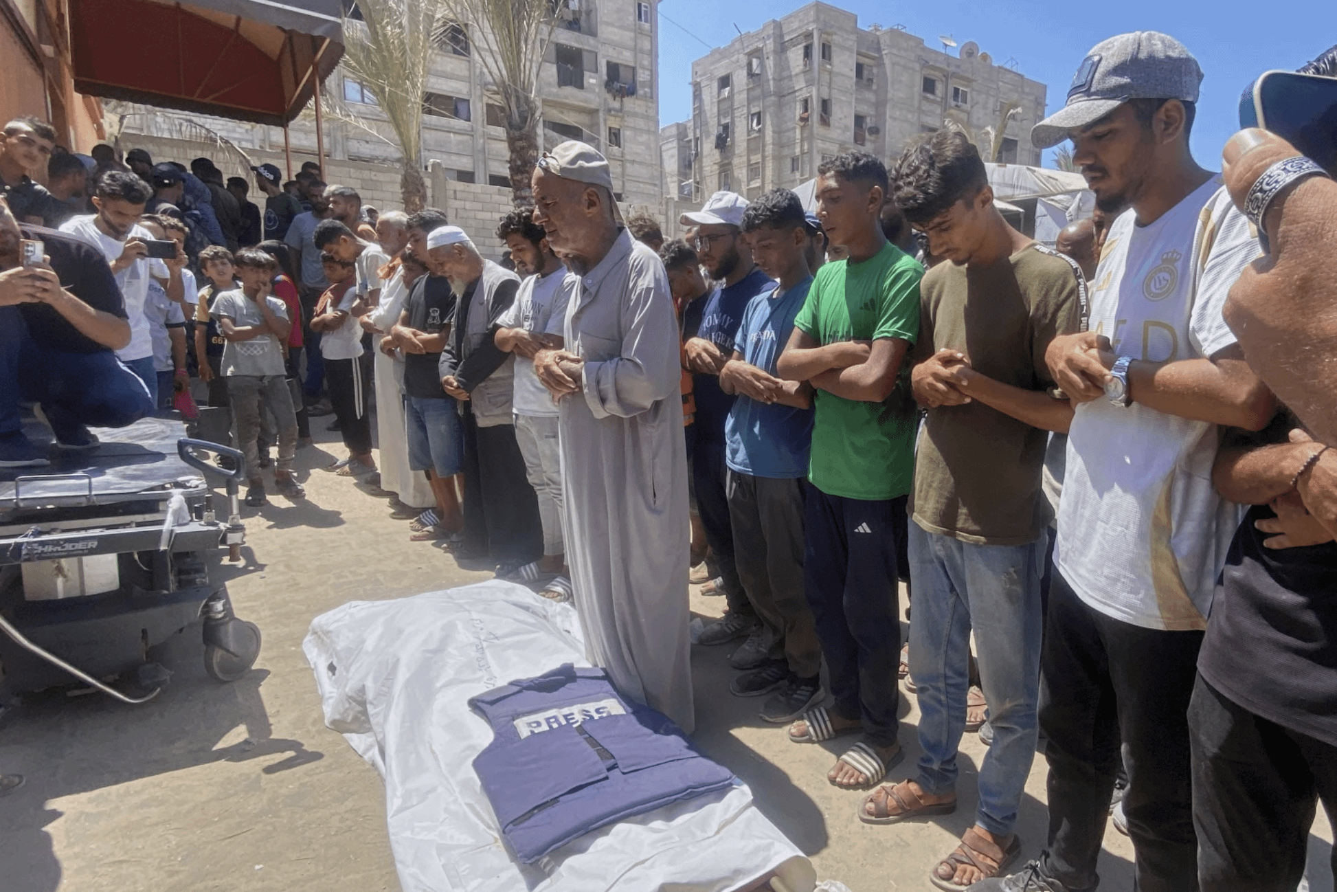 2025年8月25日，遭以色列空襲身亡的記者達加（Mariam Abu Dagga）的父親（身穿灰袍者）與親友，圍繞著達加的遺體悼念。（美聯社）