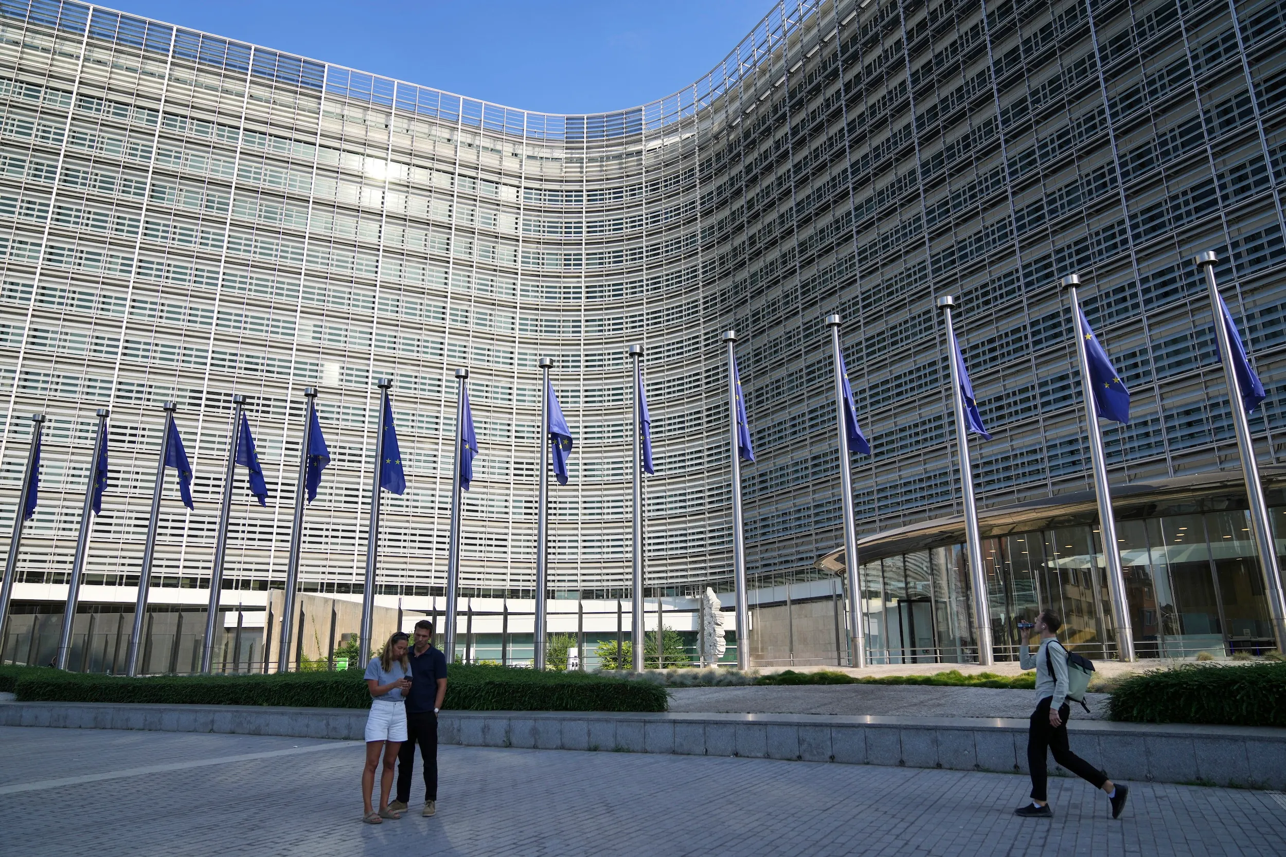2025年8月19日，比利時布魯塞爾，歐盟旗幟在風中飄揚，人們走過歐盟執委會總部前。（美聯社）