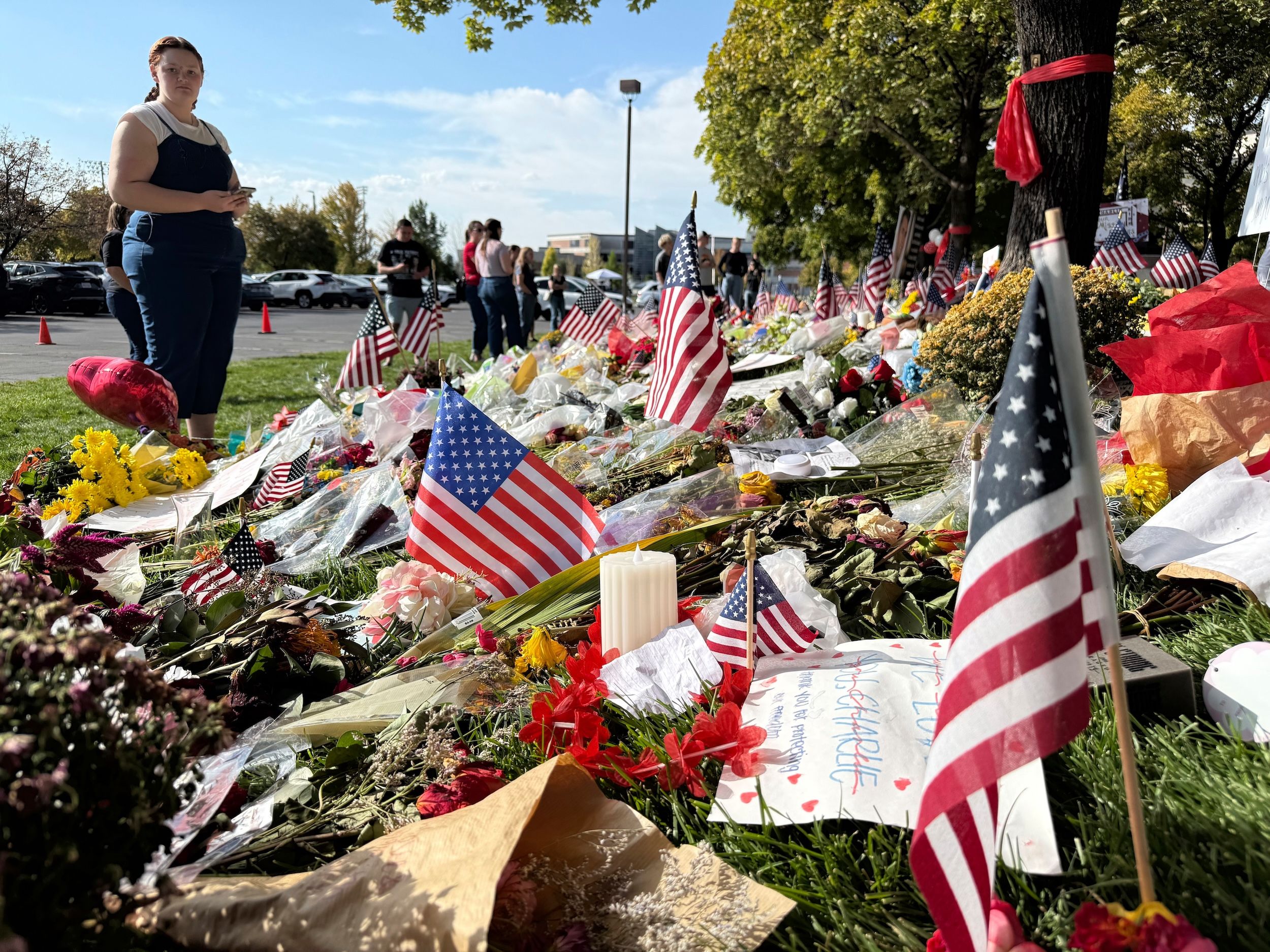 2025年9月15日、アメリカユタ州オレン、ユタバレー大学内で、チャーリー・カーク（Charlie Kirk）の記念エリアに花を捧げ、チョークで哀悼の言葉を書き残す市民たち（AP通信）