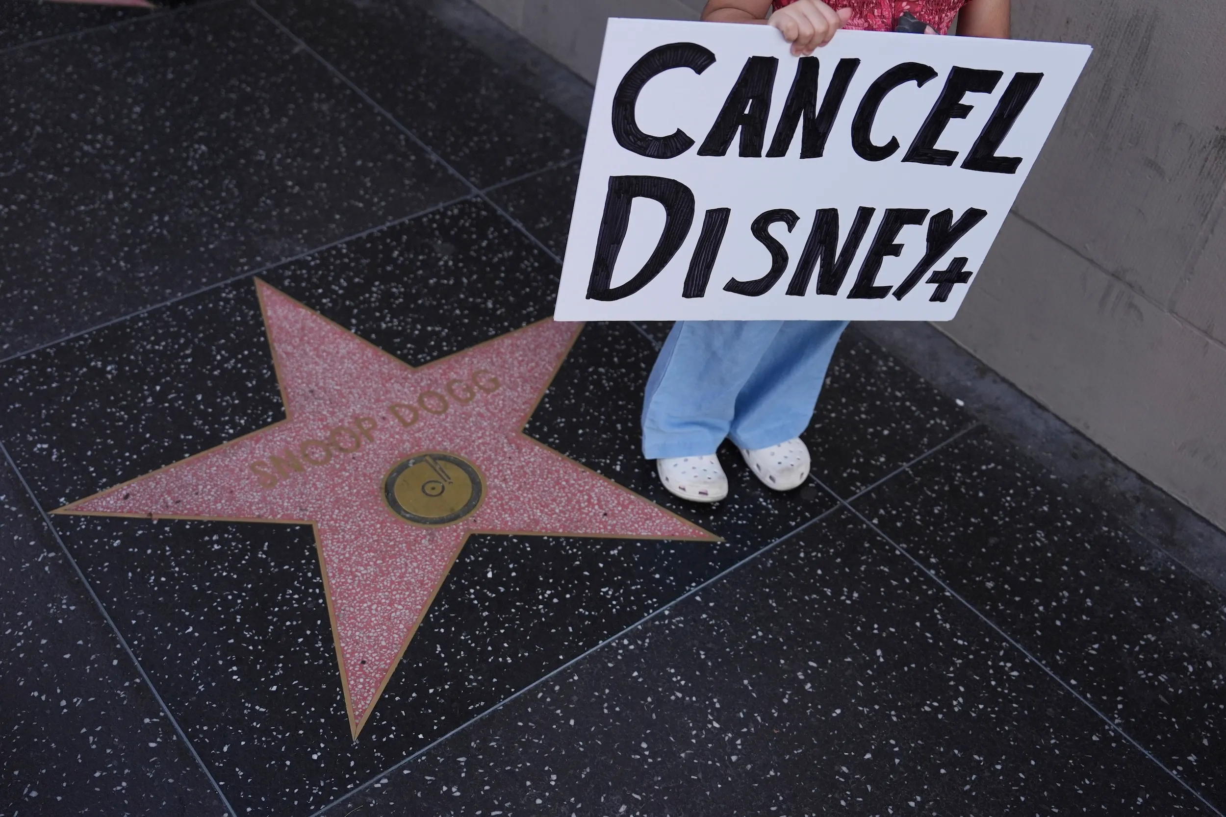 2025年9月18日，一名示威者在洛杉磯的埃爾卡皮坦娛樂中心外舉著「取消迪士尼Plus」的標語牌，此處是深夜節目《吉米·金摩現場秀》的錄製地點。（美聯社）