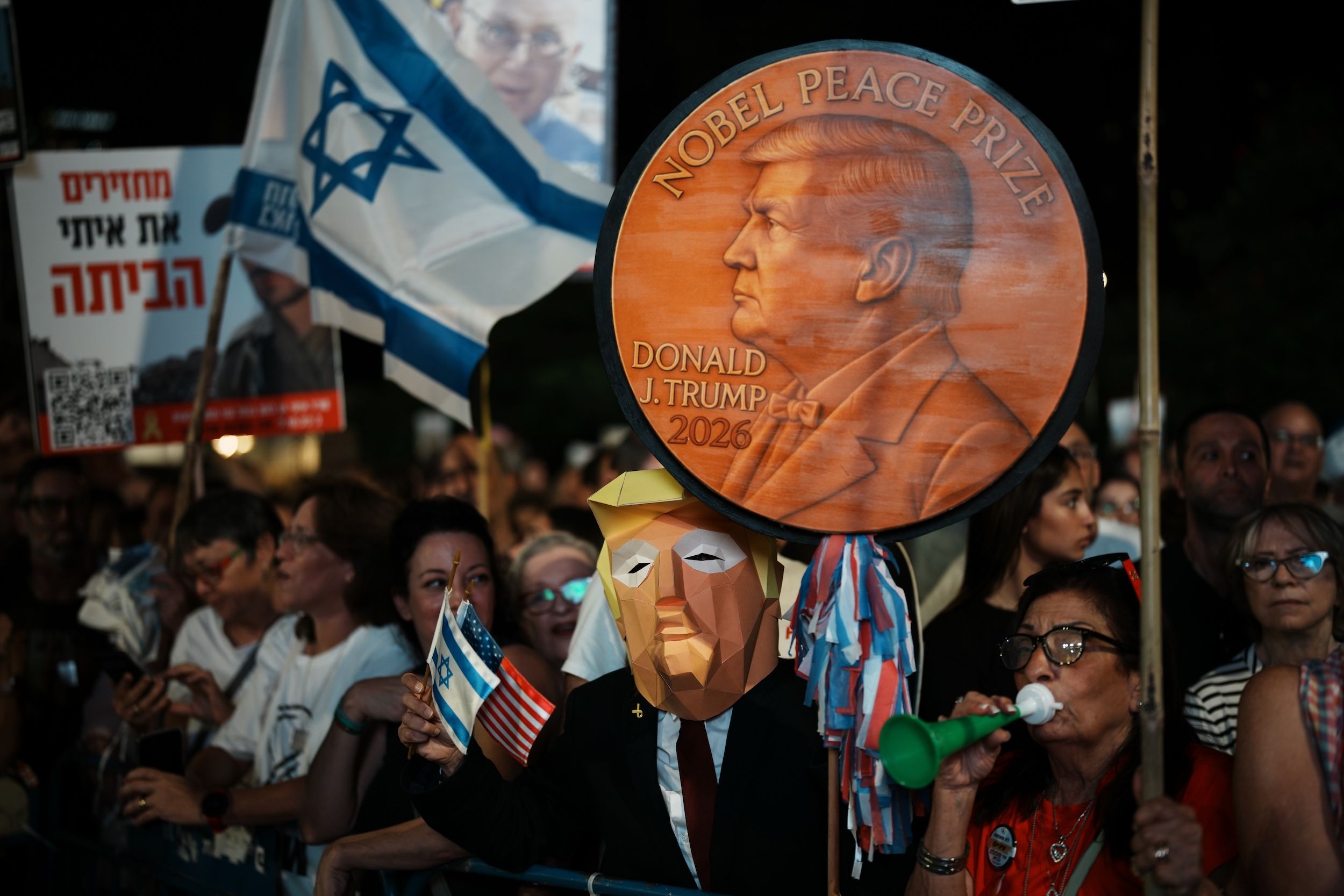 2025年10月11日、イスラエルのテルアビブで「人質広場」で行われた集会でトランプの仮面をかぶった男性が、ハマスに拘束された人質を支持してノーベル平和賞メダルを掲げる（AP通信）