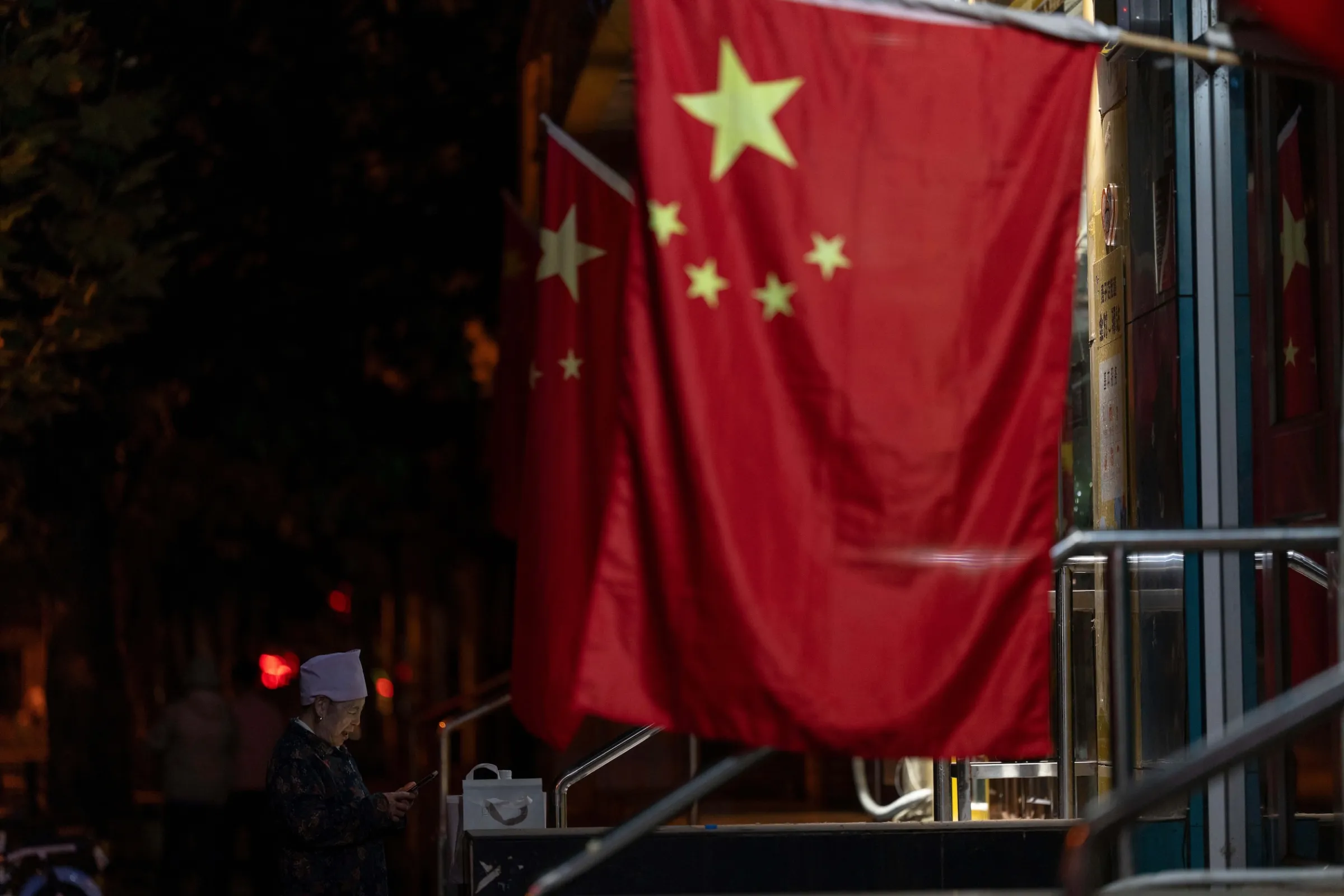 2025年10月6日，正值中秋與國慶連假期間，北京街頭掛滿中國國旗，一名老婦人站在旗幟旁。（美聯社）