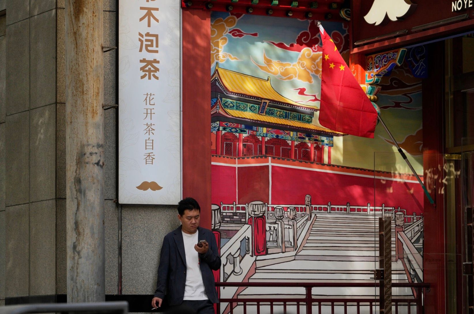 2025年10月1日，中國國慶假期期間，一名男子在描繪紫禁城的壁畫旁抽菸休息。（美聯社）