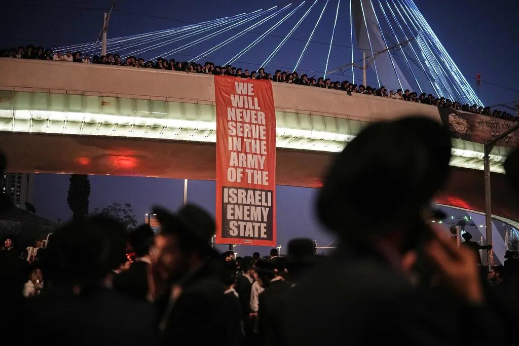 以色列正統派教徒湧入耶路撒冷街頭，抗議政府強制徵兵的決定，高掛「我們絕不入伍服役」的巨幅海報。（美聯社）