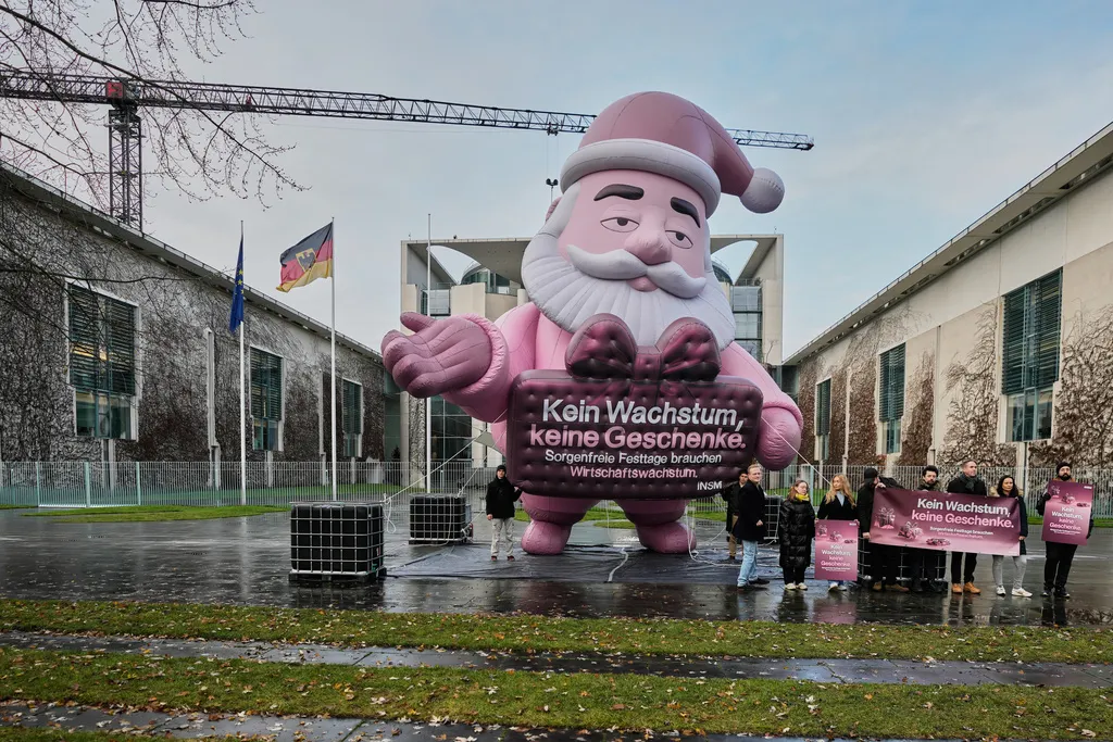 2025年12月10日。在德國柏林總理府前，一個粉紅色充氣聖誕老人手握「沒有成長。就沒有禮物。無憂無慮的假期需要經濟成長」的標語。（AP）
