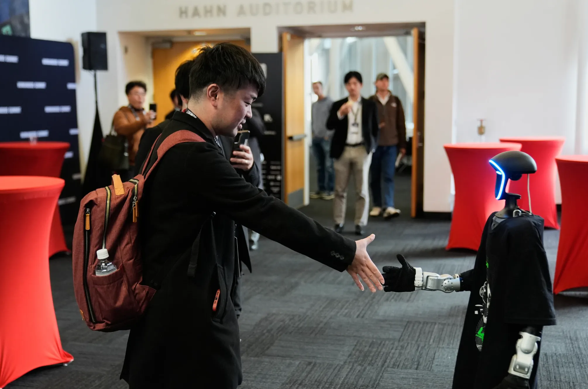 2025年12月11日，在加州山景城舉行的人形機器人高峰會上，一名男子在展場內與機器人握手。 （美聯社）