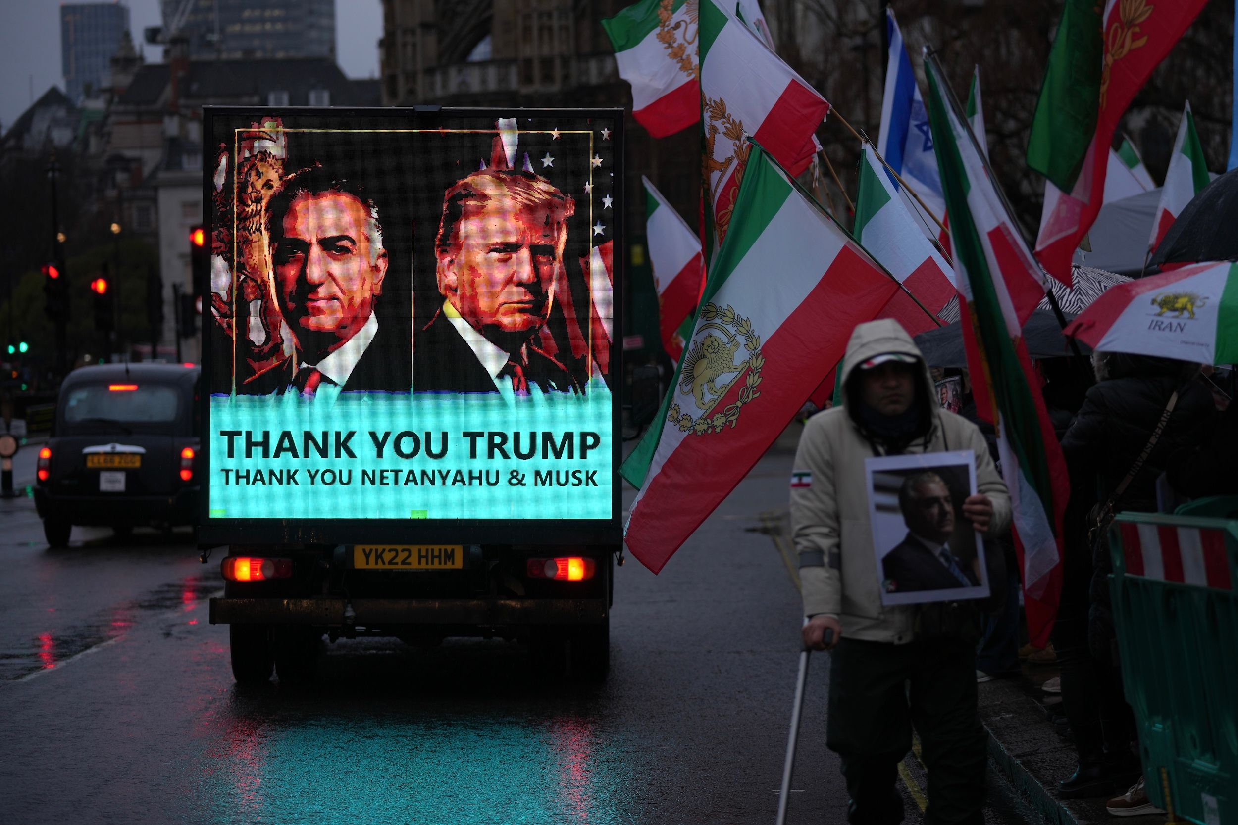 2026年1月13日，在倫敦議會大廈外，一輛汽車駛過抗議人群，車上螢幕顯示伊朗流亡王儲巴勒維（左）和美國總統川普（右）。（美聯社）