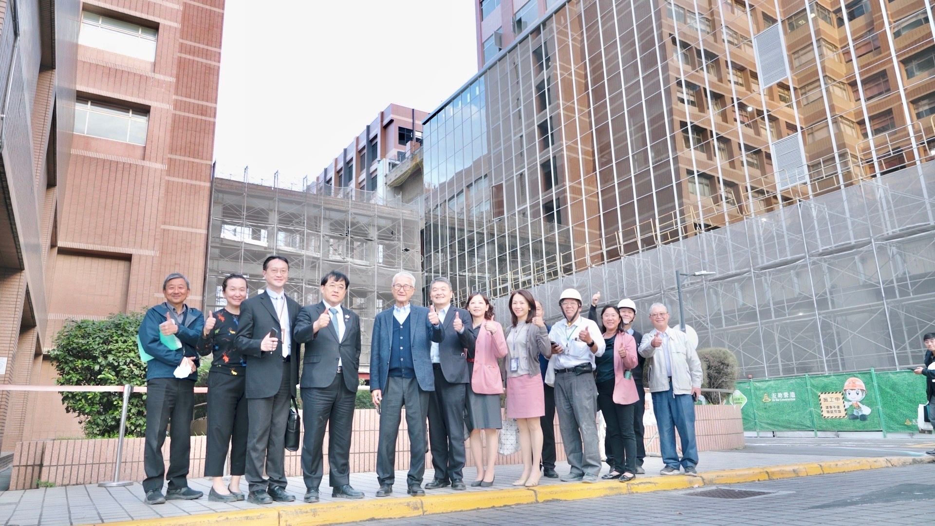 新光醫院董事長吳東進（前左3）、副院長洪子仁（前左2）與團隊在今年即將完工的桂蘭樓（右邊玻璃帷幕大樓）前合影。（新光醫院提供）