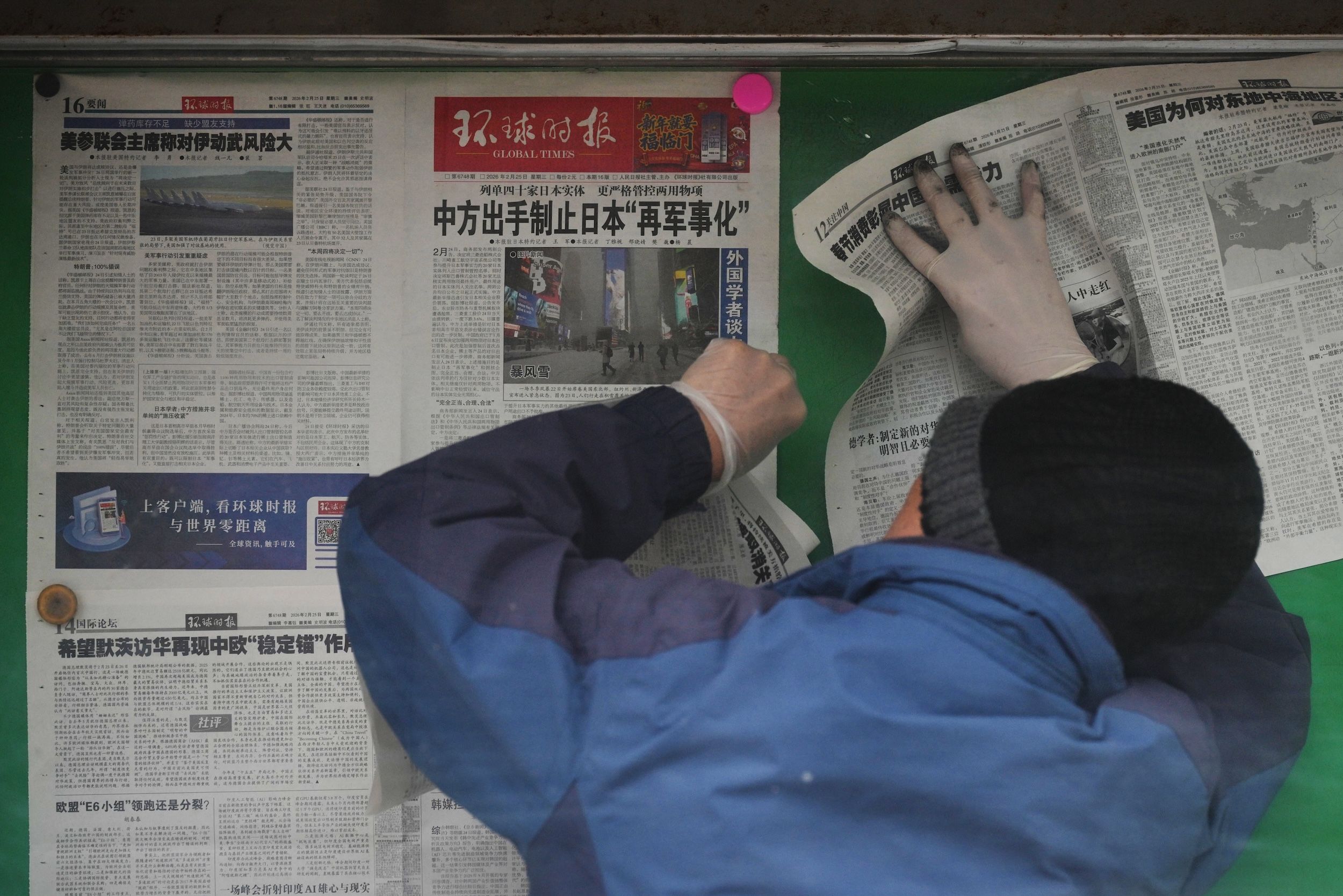 2026年2月25日，北京市民在布告欄翻閱《環球時報》。報紙頭條斜著，中國限制向40家日本實體出口，出手制止日本的「再軍事化」。（美聯社）
