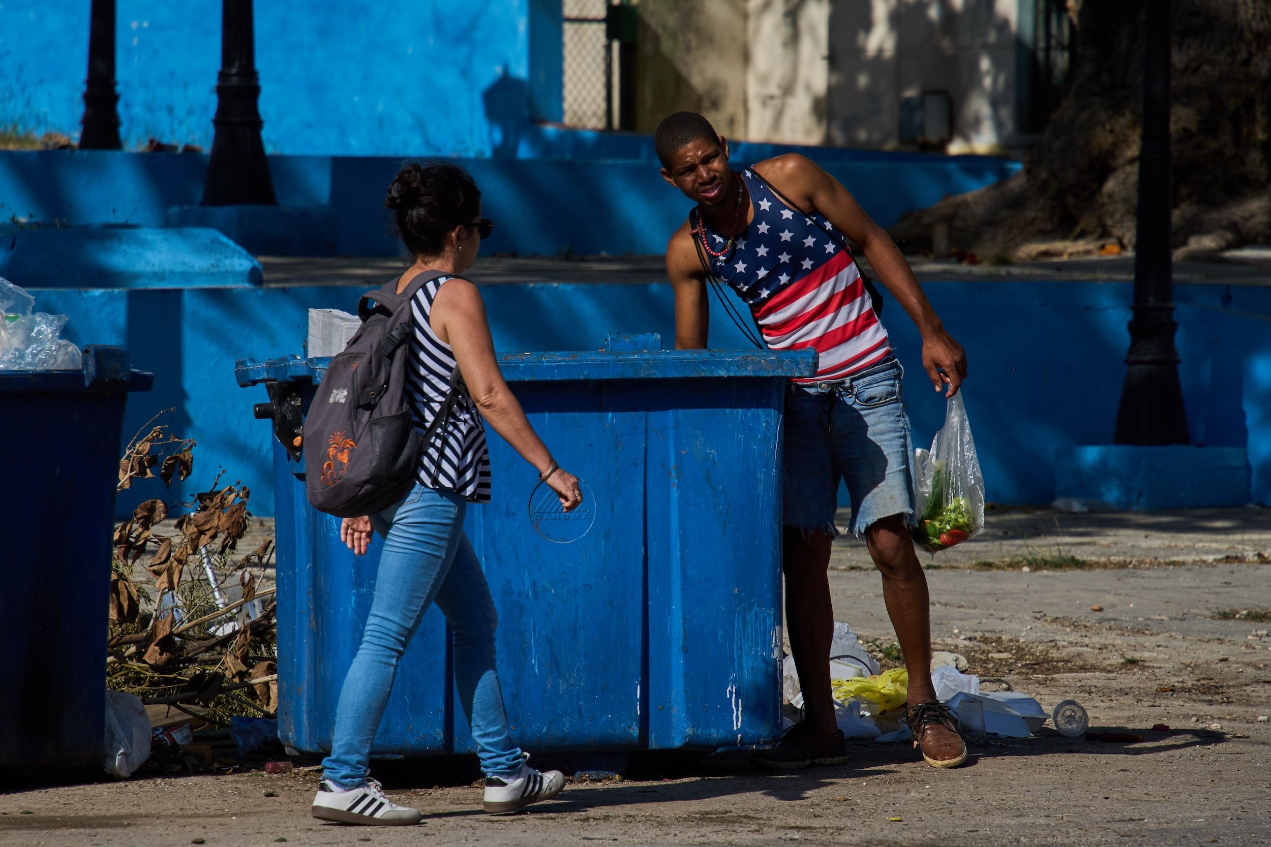 2026年3月27日，古巴哈瓦那一名身穿美國國旗圖案上衣的男子，從垃圾箱翻找食物餵豬。（美聯社）