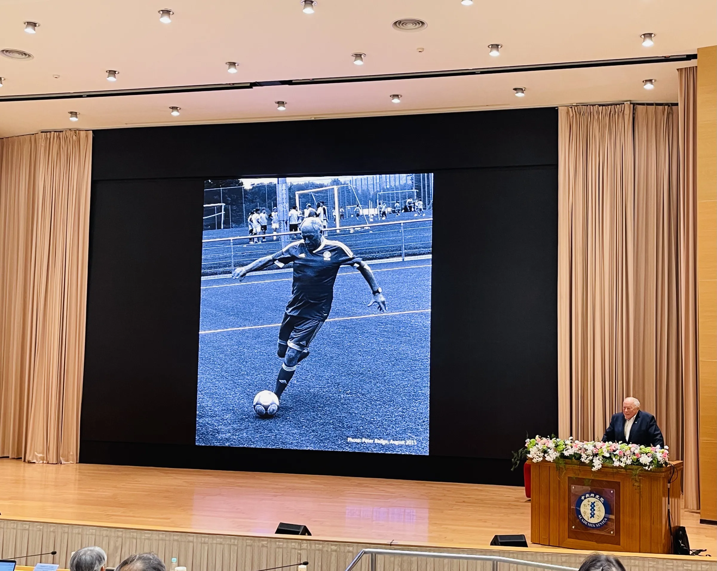諾貝爾化學獎得主Kurt Wüthrich在演講時，秀出77歲時參加國際足球總會（FIFA）表演賽，在球場上踢足球的照片。（謝錦芳攝）
