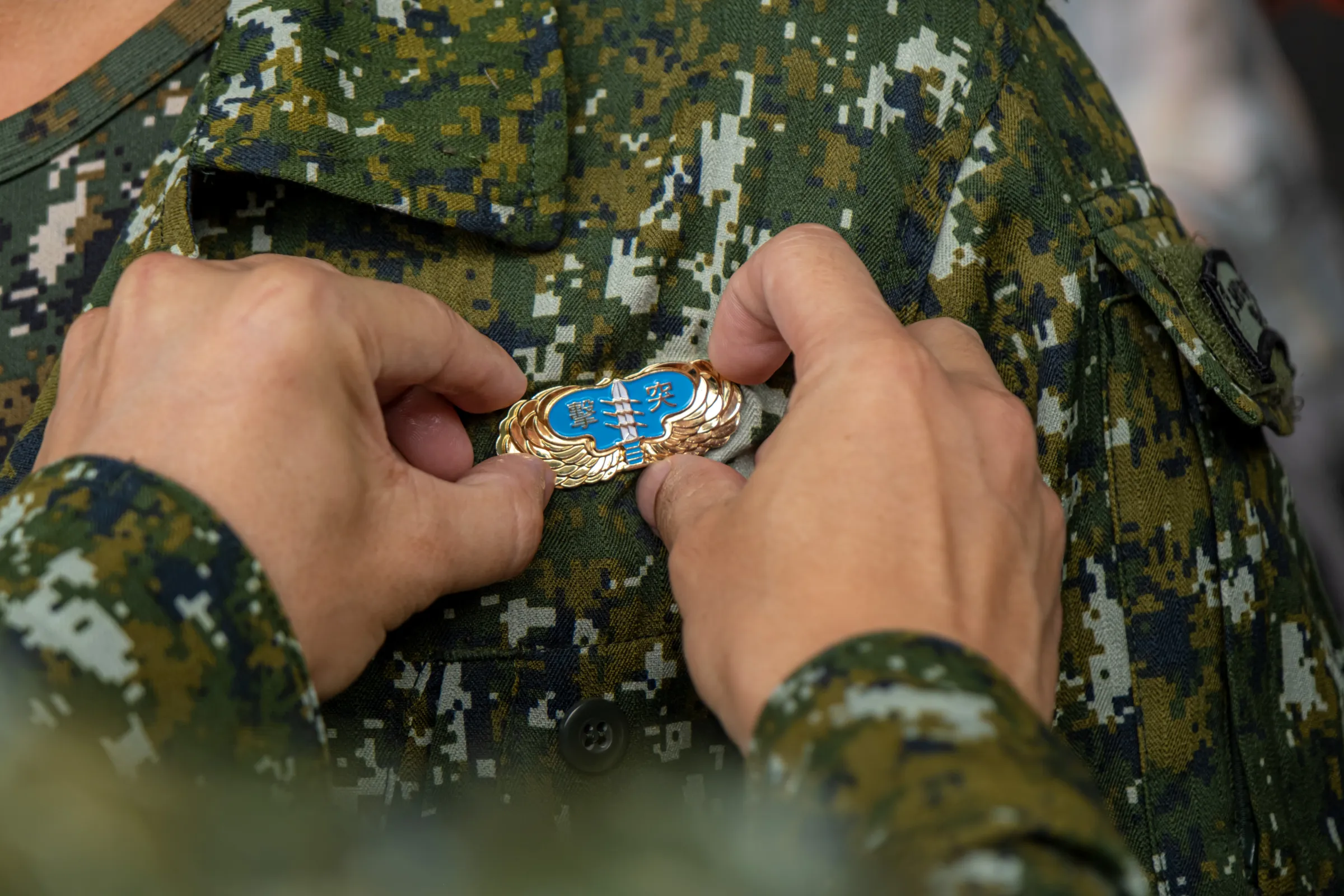 An instructor affixes a special operations badge onto a graduating trainee at the completion ceremony held at Liyang Garrison on June 12, 2026.