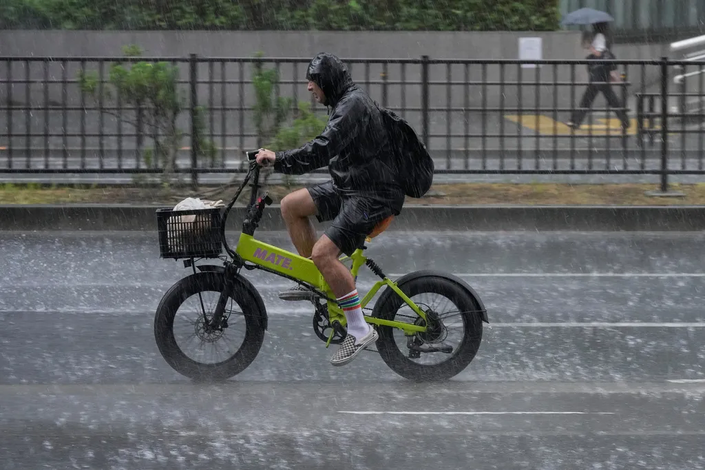 東京市區自行車騎士遭遇突然暴雨。（美聯社）