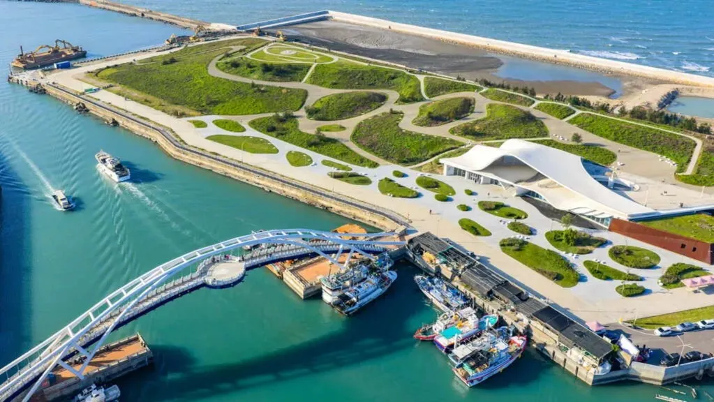 桃園景點永安漁港海螺文化體驗園區空拍景致。畫面呈現白色曲面建築、綠地步道、跨港觀海橋與停泊漁船景致。（圖／翻攝官網、桃園觀光導覽網）