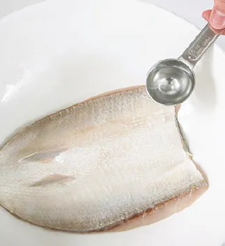 虱目魚肚洗淨，用廚房紙巾擦乾水分，再淋上米酒、鹽，去除腥味。（圖／台灣廣廈有聲圖書有限公司提供）
