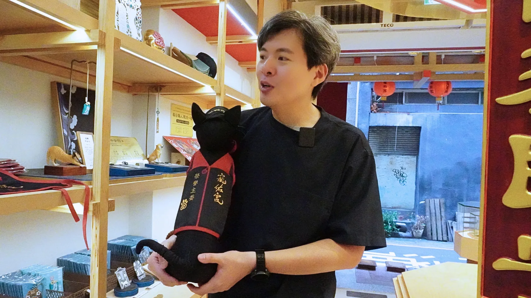 寵佑宮の11柱の神々について説明する創設者のボズ・ル氏。抱いている黒猫のぬいぐるみは、廟の「名誉主任委員」と記されたマントを着けている