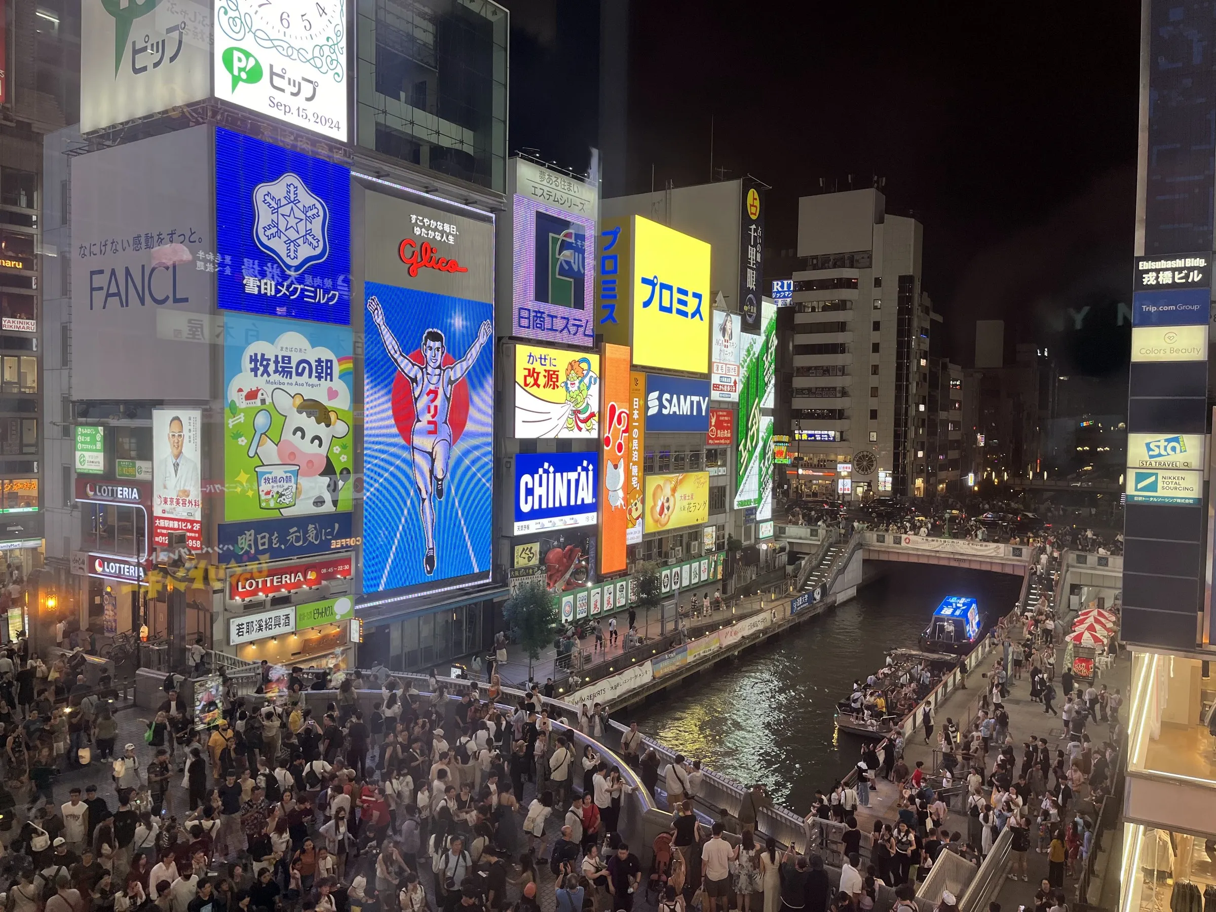從高處俯瞰大阪道頓堀河與戎橋，橋上與河岸步道擠滿觀光客，河面有觀光船經過。（溫芳瑜攝）