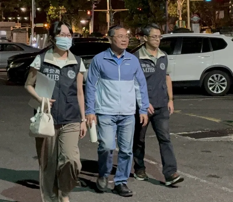 新北市議会議員・黄永昌氏が買収に関与した疑いで再聴取のため移送される様子。国民党の新北市議会議員・黄永昌氏が関廟麺を配布し買収に関与した疑いで、検察・調査当局が7日に捜索を実施し、深夜に黄氏（中央）を新北地方検察署へ移送した。検察は尋問後、公職選挙法違反の嫌疑が重大であり、証拠隠滅の恐れがあると認定し、裁判所に接見禁止を伴う逮捕状を請求した。中央社記者曹亜沿撮影 115年10月8日