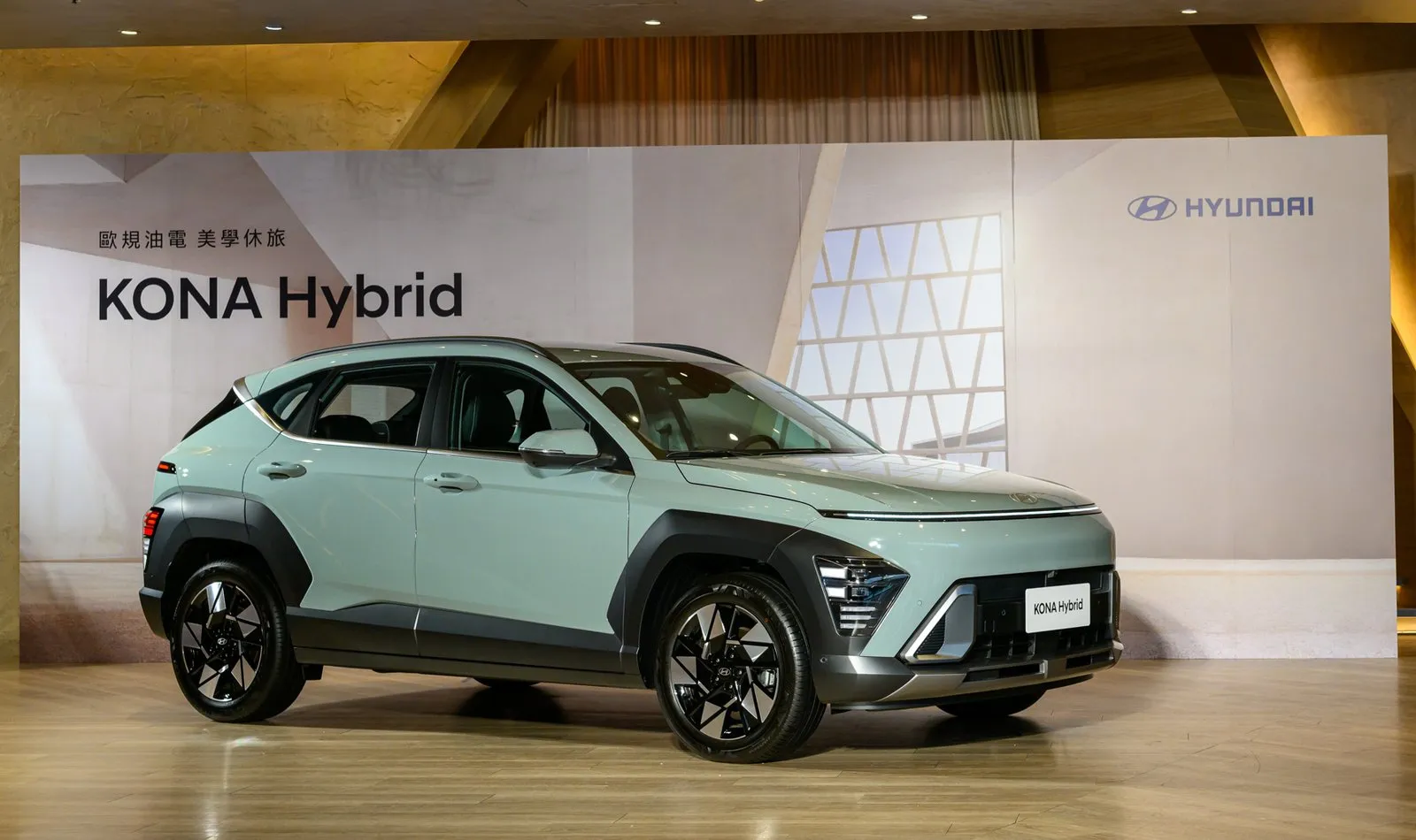 淺綠色 HYUNDAI KONA Hybrid 休旅停駐於發表會舞台，背板印有「歐規油電 美學休旅」字樣